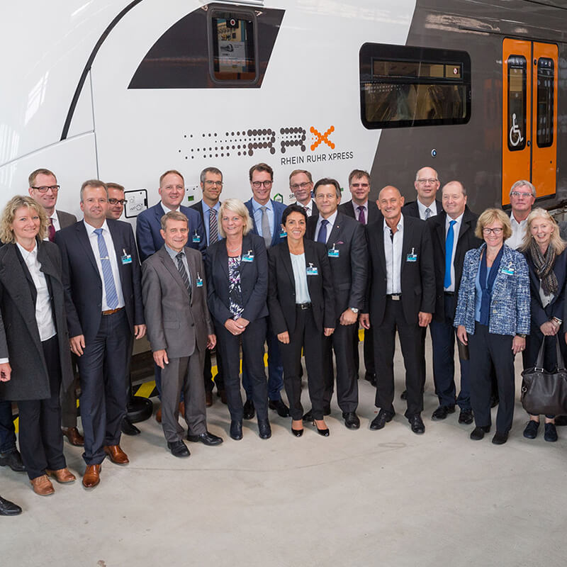 Eine große Anzahl von Projektpartnern des RRX posiert vor einen RRX in der Werkshalle von Siemens.